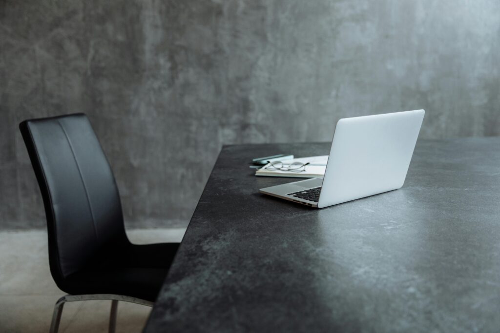 A sleek workspace featuring a laptop on a gray table with a leather chair, creating a minimalist office vibe.