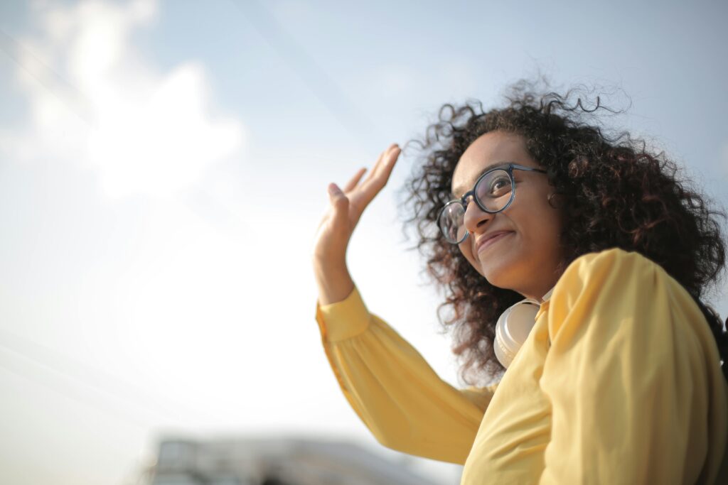 Cheerful woman in yellow waves hello with a bright smile on a sunny day.